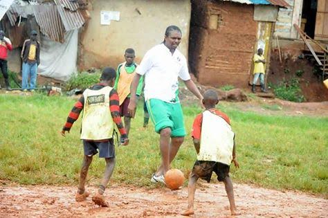 Kanu Nwankwo pictured playing football with kids on a muddy field in Uganda theinfong.com